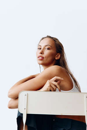 Portrait of a beautiful woman in a chair with beautiful tanned skin and a smile on the white wall of...