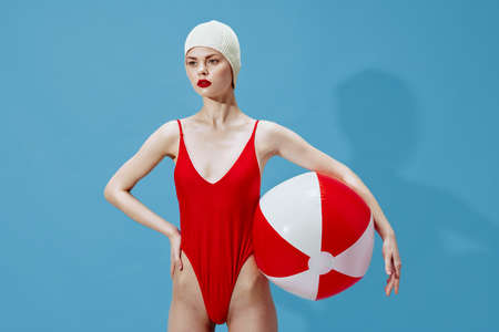Fashion concept art. Woman in a red swimsuit swim cap with a striped ball on her hipの写真素材