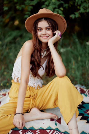 Beautiful young girl close-up looks into the camera in a hat wearing an eco hippie outdoors, beautiful smile with teeth in the sunset lightの写真素材