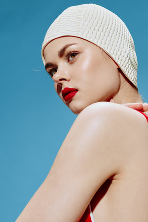 Close-up portrait. A conceptual stylish woman in a swimming cap in a red swimsuit looks to the side on a blue background. The new generation of fashionの写真素材