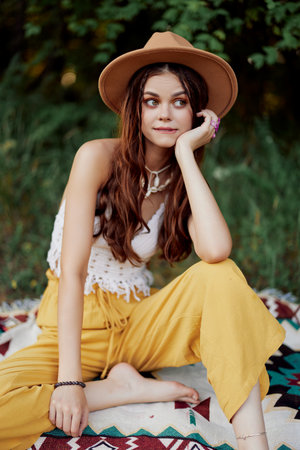 Beautiful young girl close-up looks into the camera in a hat wearing an eco hippie outdoors, beautiful smile with teeth in the sunset lightの写真素材