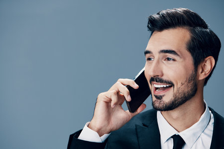 Portrait of business man with phone conversation and smile with teeth on blue background in business suit. Business portrait of a stylish man copy spaceの写真素材