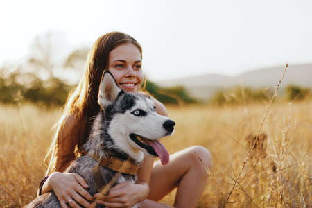 Woman and her husky dog happily stroll through the grass in the park smile with teeth fall sunset walk with pet, travel with a dog friendの写真素材