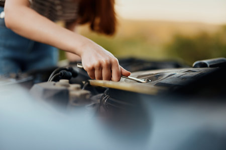 A woman traveler stands by her old car with the hood open and repairs the car engine with a wrenchの写真素材