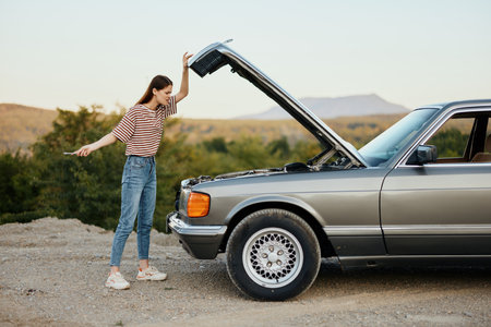 A woman opened the hood of a broken down car and tries to find the cause of the breakdown on the road during a nature trip alone.の写真素材