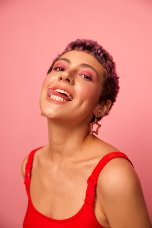 Fashion portrait of a woman with a short haircut of purple color and a smile with teeth in a red top...
