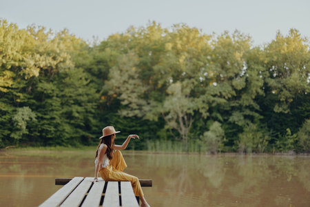 A young happy hippie woman sitting on the lake shore on a bridge in eco clothing made of natural materials in harmony with nature in the fallの写真素材