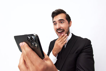 Man businessman holding the phone and smiling happily with teeth of surprise. Trading and winning at casinos online via phone. Close-up wide angle photo white isolated backgroundの写真素材