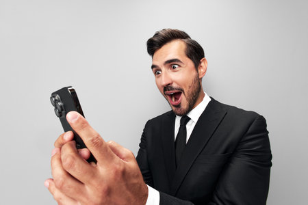 Man businessman in suit holding phone in hand on phone posing in front of smartphone camera with smile with teeth happy surprise win on gray background close-up face wide camera angle, technologyの写真素材