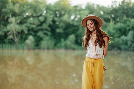 A young woman in a hippie look travels in nature by the lake wearing a hat and yellow pants in the fallの写真素材