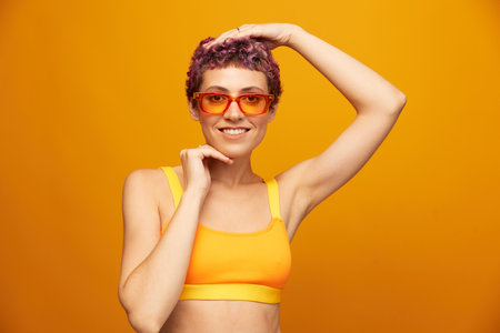 Young woman in a bright yellow fitness tracksuit with an open belly and sunglasses on an orange...