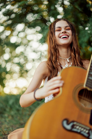 A young hippie woman with a guitar in her hands smiles sweetly into the camera on a trip to nature lifestyle in harmonyの写真素材