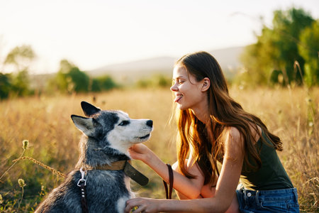 Woman walking her husky dog and smiling happily with teeth on a nature walk on the grass in the autumn sunset, lifestyle dog friendの写真素材