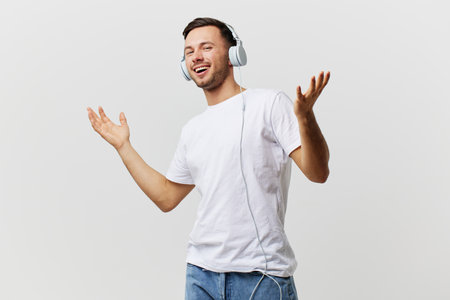 Happy smiling tanned handsome man in basic t-shirt headphones raise hands up greeting someone posing isolated on over white studio background. Copy space Banner Mockup. Favorite song conceptの写真素材