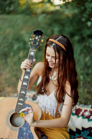 Happy hippie woman with a guitar relaxing in nature sitting on a plaid smiling and enjoying the view. Lifestyle in harmony with nature and selfの写真素材