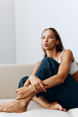 A woman sits relaxed on the couch and smiles looking at the camera in home clothes with long hair...