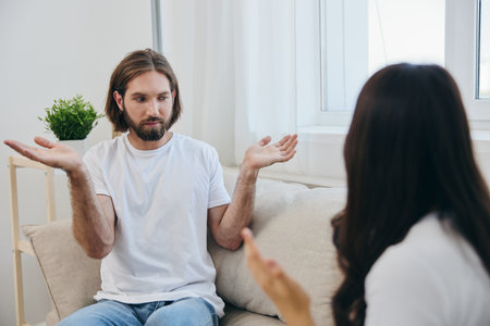 A man and a woman sit on the couch at home in white T-shirts and chatting scandalously do not...