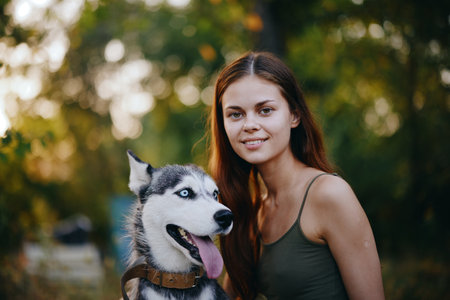 A woman with a husky breed dog smiles and affectionately strokes her beloved dog while walking in...