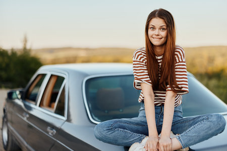 A young woman sits on the hood of her car and laughs with her eyes closed, a journey from a noisy...