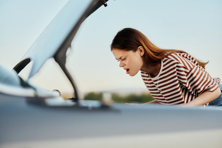 A sad woman looks in disbelief at her broken down car on the road while traveling and does not know what to doの写真素材