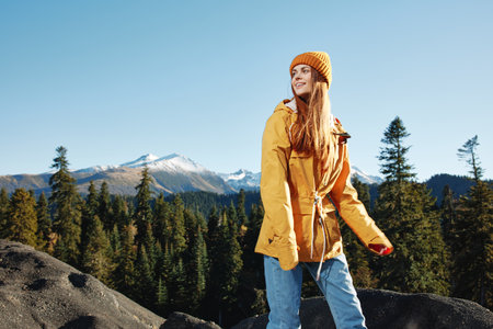 Woman smile with teeth happiness and laughter hiker in yellow raincoat put her hands up and jumping trip in the fall and hiking in the mountains in the sunset freedomの写真素材