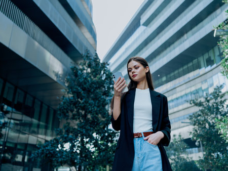 Portrait of a stylish young business woman in a jacket with a phone in her hands, stock market cryptocurrency, online trading, buying stocks of companiesの写真素材