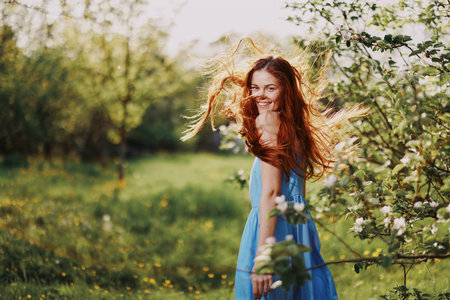 Woman with a beautiful smile with teeth and long hair flying hair spring dance hands up in the sunset in the park near the flowering trees happiness, natural beauty and hair healthの写真素材
