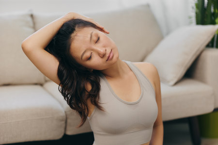 Young Asian woman in front of her laptop sports and yoga repeating exercises on the video at home in lotus position stretching the muscles of the neck, a set of home workouts for the body lifestyleの写真素材