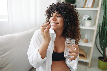 Pregnant woman smile blogger takes vitamins and medicines pills with a glass of water close-up...