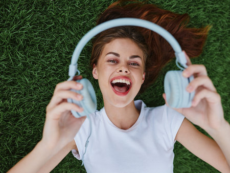 Teenage girl lying on the grass and holding out her headphones for the camera smile with her teeth, fun summer vacationの写真素材