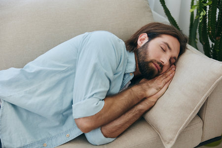 A man sleeping on the couch during the day is tired and relaxed after stress and feeling bad. Stress at work, poor sleep and health problemsの写真素材