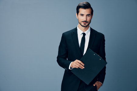 Portrait of a business man in a stylish suit smile with tie beautiful face on a blue isolated background with a tablet in his hands. Business concept young businessman startup copy placeの写真素材