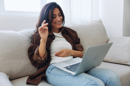 Woman freelancer on day off sitting on sofa with laptop at home online video chat call, smileの写真素材