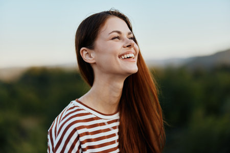 Close-up portrait of a young woman with a beautiful smile with teeth in a striped t-shirt against the background of treesの写真素材