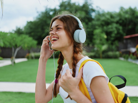 Happy teenage girl listening to music with headphones with a backpack in a white T-shirt and walking to college to study on the street smiling with teeth, student lifestyleの写真素材