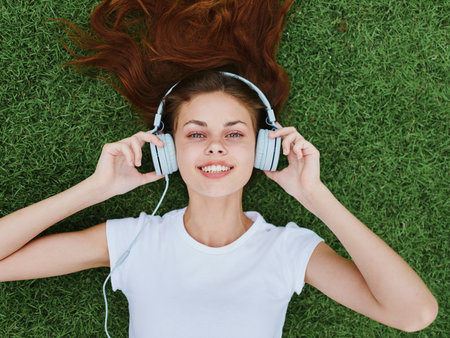 A woman lying on the green lawn listening to music in headphones in a white T-shirt, a smile with teeth happinessの写真素材
