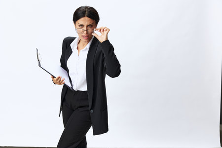 Business woman with a folder of documents in her hands in a black business suit and glasses shows signals gestures and emotions on a white background, work freelancer online trainingの写真素材