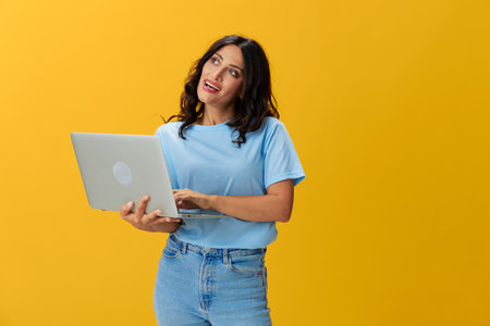 Woman freelancer with a laptop in her hands in a blue t-shirt and jeans on a yellow background smile signs gestures symbols, copy space, free backgroundの写真素材