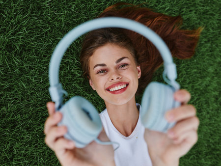 Teenage girl lying on the grass and holding out her headphones for the camera smile with teeth, funの写真素材
