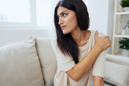 Woman sitting on sofa at home arm and shoulder pain, muscle sprain and joint pain, calcium problems...