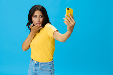 Woman with a phone in her hands with a yellow case on a blue background in a yellow T-shirt,...