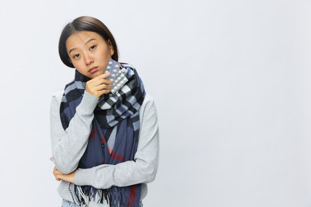 Asian woman headache cold flu holding medicine and pills in checkered plaid with fever sick of virus...