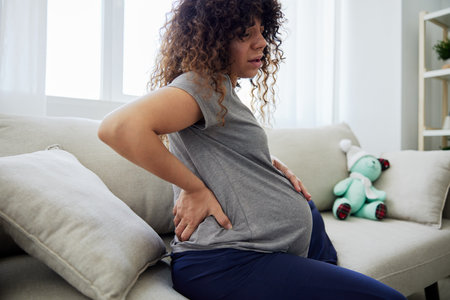 Pregnant woman sitting on the couch lower back pain and headache, strain on the spine during pregnancy. Lifestyle preparation for childbirth, last month of pregnancyの写真素材