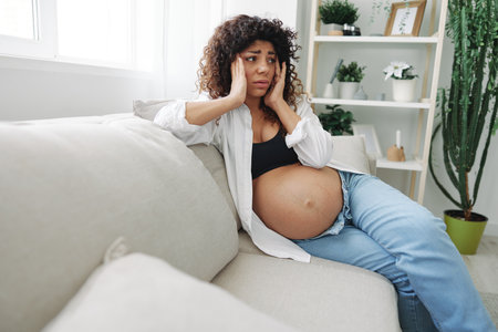 Pregnant woman headache lies at home on the couch fatigue and heaviness in the last month of pregnancy before childbirth, motherhood difficultiesの写真素材