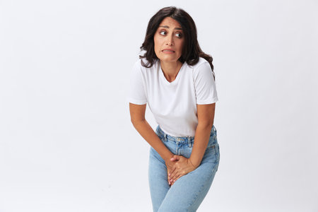 Woman pain during menstruation, abdominal pain appendicitis, age problems, early menopause, cystitis, a woman in a white t-shirt on a white background in jeans, copy spaceの写真素材