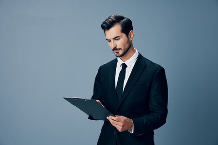 Portrait of a business man in a stylish suit smile with tie beautiful face on a blue isolated background with a tablet in his hands. Business concept young businessman startup copy placeの写真素材