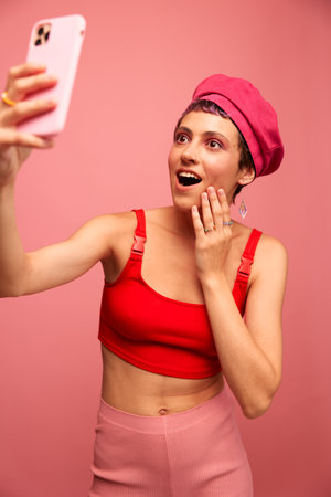 A young woman blogger with colored pink hair and a short haircut takes a picture of herself on the...