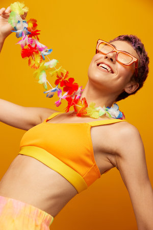 Woman with floral Hawaiian wreath around her neck has fun dancing and smiling in bright clothes on orange background with sunglasses, lifestyle party in Hawaiian styleの写真素材