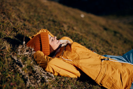 Woman beautifully lying on a hill recreation smile with teeth in the mountains in the autumn in a yellow raincoat and jeans happy sunset trip to hike the mountains in the snow, freedom lifestyleの写真素材