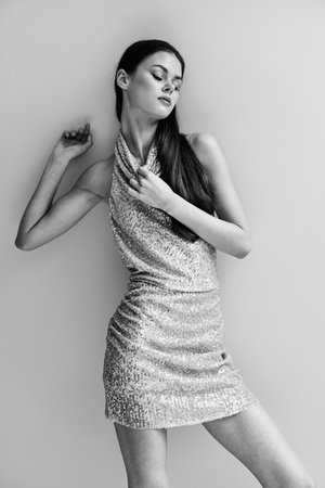 Black and white photo of a woman in a stylish sequined party dress posing near a wallの写真素材